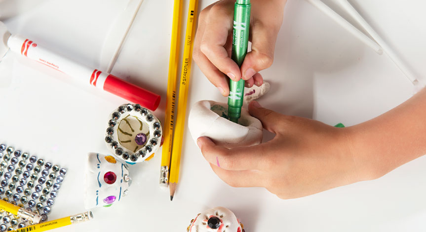 A child coloring the inside of their Model magic design using crayola markers. two pencils on the table.